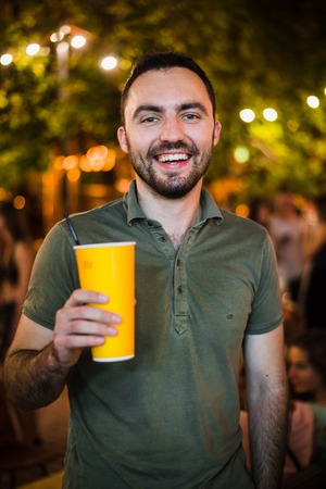 Handsome Bearded European Man Drinking coctail or beer at outdoor Street Cafe or night party in park.の写真素材