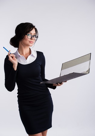 Young Caucasian woman wearing a dark blue dresst and and a white shirt, holding a ring binder folder and pen. Isolated on light backgroundの写真素材