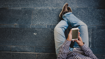 young Man with the phone in his hand sitting on the steps. top view.