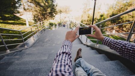 Close up of a man taking photos of view with his smart phone while sitting on a stairs.の写真素材