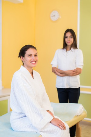 Woman beautician doctor with patient in spa wellness center. Young female professional cosmetologist made massage to beautiful brunette girl in cosmetology cabinet or beauty parlorの写真素材