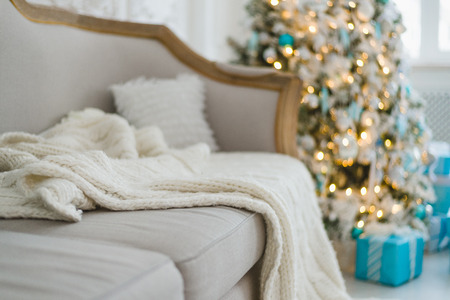 Christmas or new year decoration at Living room interior and holiday home decor concept. Calm image of blanket on a vintage sofa with tree and gifts. Selective focus.の写真素材