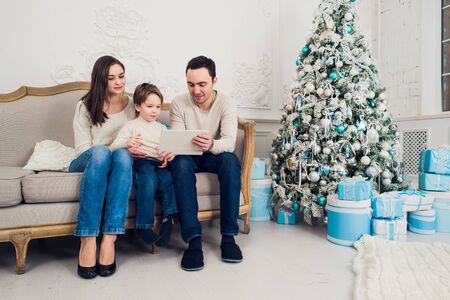 Cheerful family sitting in the living room having fun with the digital tablet that Santa Claus brought her, behind the decorated christmas tree.の写真素材