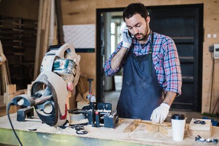 portrait of carpenter calling by smart phone at the workshop.