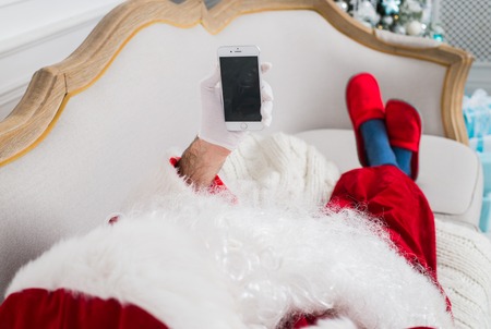 Santa claus using mobile phone at home during christmas time.の写真素材