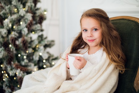 10 years old preteen girl in pajama laying on carpet with holiday bedding by Christmas tree and fireplace and drinking milk in morning at homeの写真素材