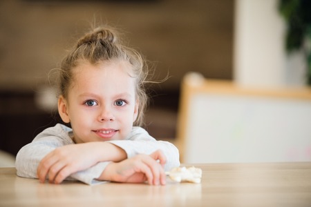 Beautiful calm little girl sitting at wooden table.の写真素材