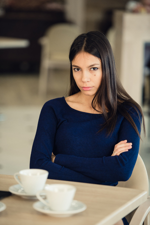 Angry young woman with crossed arms at cafe.の写真素材