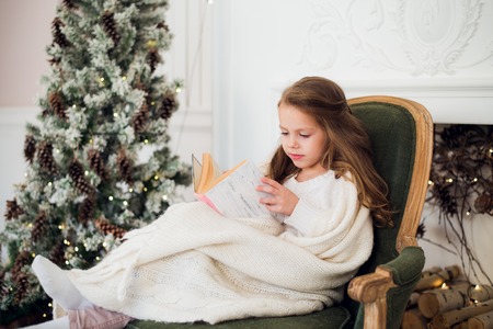 Little girl reading book near Christmas tree.の写真素材
