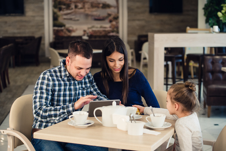 family, parenthood, technology and people concept - happy mother, father and little girl with tablet pc computer having dinner at restaurant.の写真素材