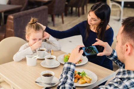 leisure, technology, lifestyle and people concept - happy family with smartphone taking picture of food at restaurant.の写真素材