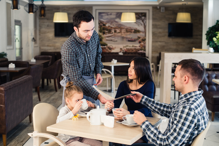 restaurant and holiday concept - waiter giving menu to happy family at restaurant.の写真素材
