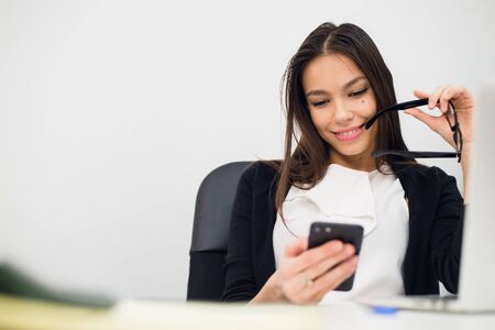 Excited businesswoman winning after achievement reading a smart phone sitting in a desktop at...