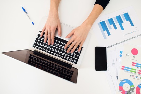 Laptop with women hand and paper graph on white tableの写真素材