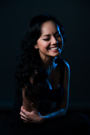 Studio shot of a beauty girl laughing with arms crossed on the dark background.の写真素材