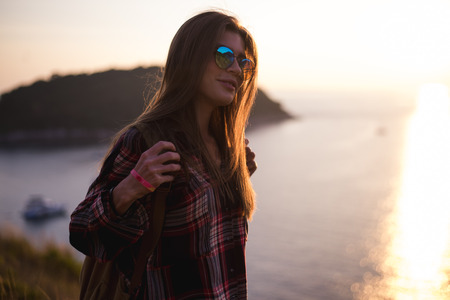 Young stylish hipster girl enjoy sunset on viewpoint. Travel woman with backpackの写真素材
