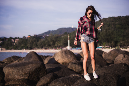 Outdoor summer stylish portrait of beautiful elegant woman with perfect fit body and long legs walking along on the beach,wear summer outfit, posing at sunny day on the beach of sandの写真素材