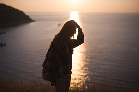 Hipster stylish woman traveler looking on a sea or ocean at the sunset