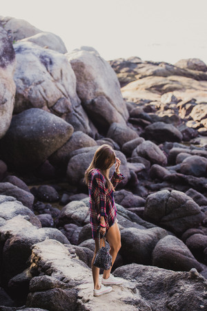 Stylish hipster woman in checkered shirt and shirts on summer beach at sunset. Path in a rocks at beachの写真素材