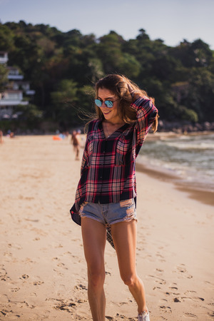 Summer sunny lifestyle fashion portrait of young stylish hipster woman walking on beach,wearing cute trendy outfit, travel, hikes, smiling enjoy her weekendsの写真素材