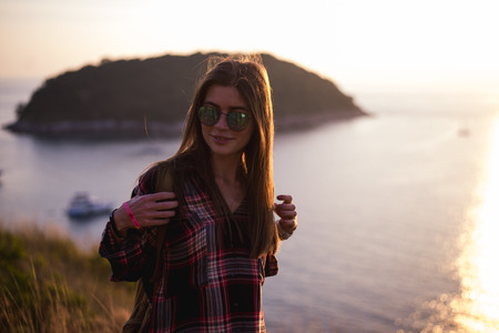 Young stylish hipster girl enjoy sunset on viewpoint. Travel woman with backpackの写真素材
