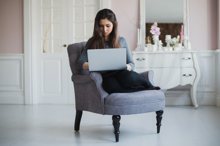 Young woman at home in the armchair relaxing in her lliving room with laptopの写真素材