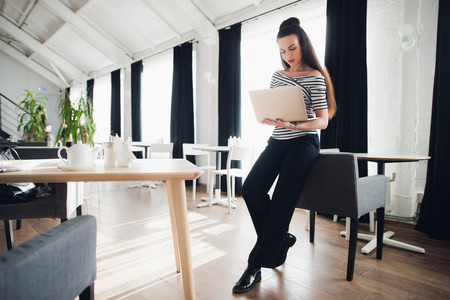 Young attractive brunette woman holding a laptop and typing, while looking at the screen.の写真素材