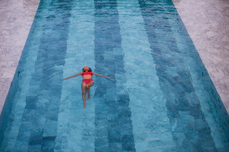 Top view aerial photo of a seductive sexy model in white swimwear is enjoying relax in hotel pool during her summer weekend. Amazing fashion woman in bikini having luxury spa restの写真素材