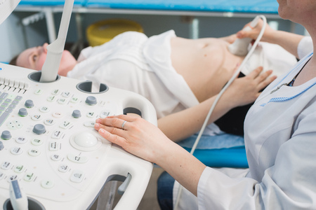 Close up of incognito doctor using ultrasound equipment for screening pregnant woman and press on...