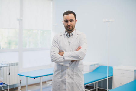 Portrait of a serious confident male doctor standing with arms crossed at medical officeの写真素材