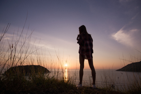Woman traveler looks at the edge of the cliff on the sea bay of mountains in the background at...