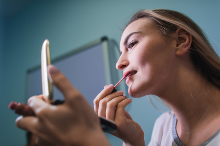 Young woman applying lipstick looking at mirrorの写真素材