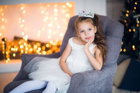 Cute little girl in smart white dress Christmas around the fireplace which decorated with holiday garlandの写真素材