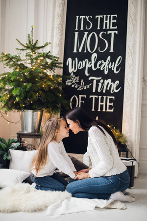 Close-up photo of little girl in knitted sweater kiss her mother while sitting on sofa at Christmasの写真素材