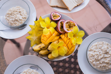 Delicious home breakfast served for three person. Oatmeals porrige and fruit bowl with mango,...