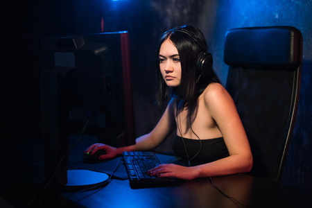 A woman looks at camera while sitting in front of her PC and playing online computer games and streaming game on the internet. Gamer girl plays at the table in his room.の写真素材