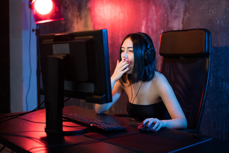 Terrified gamer plays games on your computer. An emotional young woman in the headphones plays games on a computer. Gamer concept.の写真素材