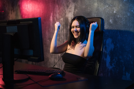 Happy cheerful cute sexy gamer girl hand gesture of win and pure emotion. Sitting at home playing video games alone on a pc computerの写真素材