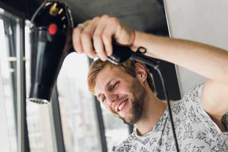 Male hairdresser smiling and talking with a customer while making a new haircut to beutiful young brunette womanの写真素材