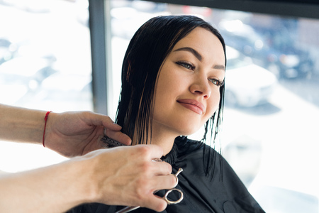 Happy young woman getting a new haircut by hairdresser at parlorの写真素材