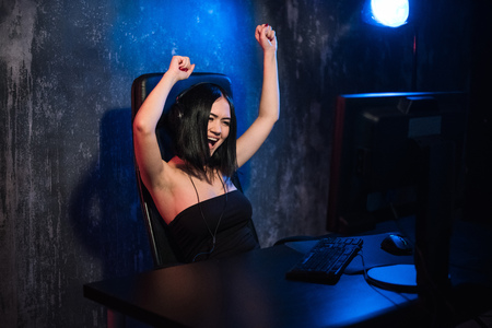 Portrait of ecstatic gamer girl in headphones screaming and rejoicing while playing video games on computerの写真素材