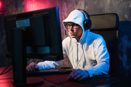 Professional Boy Gamer Plays in Video Game on a eSports Tournament or in Internet Cafe. He Wears Headphones and Speaks Commands into Microphone.の写真素材
