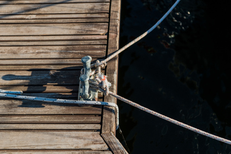 Yachting detail, rope and mooring double cross bollard on bridge in port of sailing. Wooden pierの写真素材