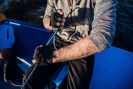 Close up of sailor winds aroung rope by using handle for coiling. He works with both hands. Young man stands on yacht. He is strongの写真素材