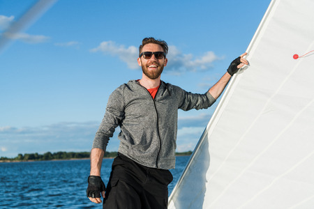 Young european man standing at edge of yacht looking at sea. Travelling on old boat with sail. Luxury lifestyle.の写真素材