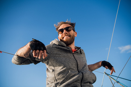 Man wearing sunglesses sitting in a sailing vessel feeling happy in the open sea and blue sky above