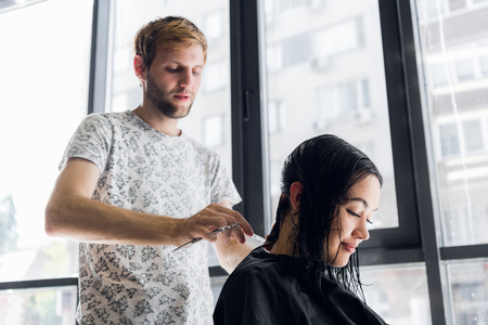 Hairdresser cutting clients hair in salon with scissors closeup. Using a combの写真素材