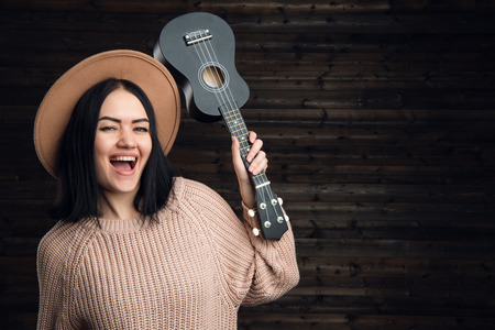 happy girl with small ukulele guitar shout. Brunette woman having fun with guitarの写真素材
