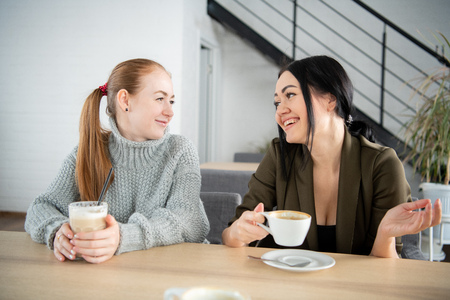 Two women are holding coffee mug. Sitting on the couch talking about the job in the morning. One cup of coffee will make the body and brain fresh.の写真素材