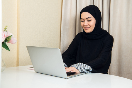 elegant attractive muslim woman using mobile laptop searching online shopping information in living room at homeの写真素材